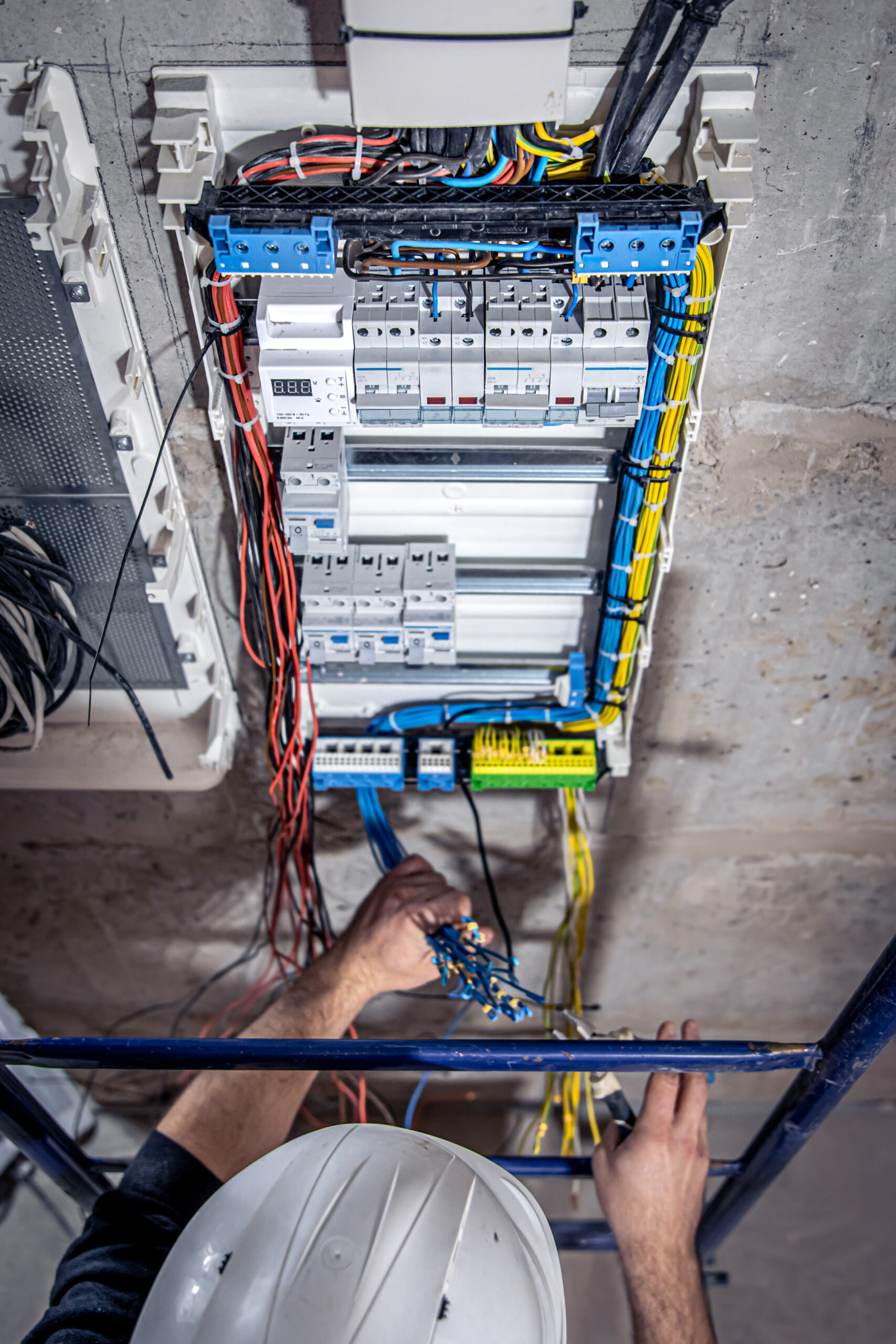 a male electrician works in a switchboard with an electrical connecting cable.